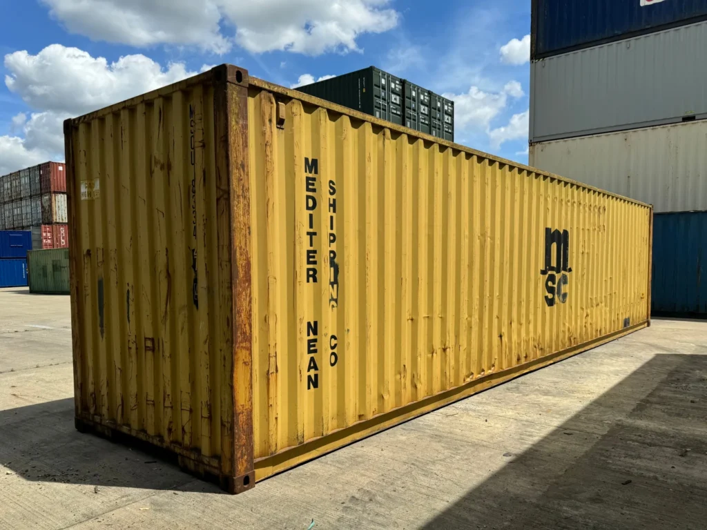 40ft used high cube yellow shipping container with rust marks, photographed outdoors in a storage depot under blue sky.