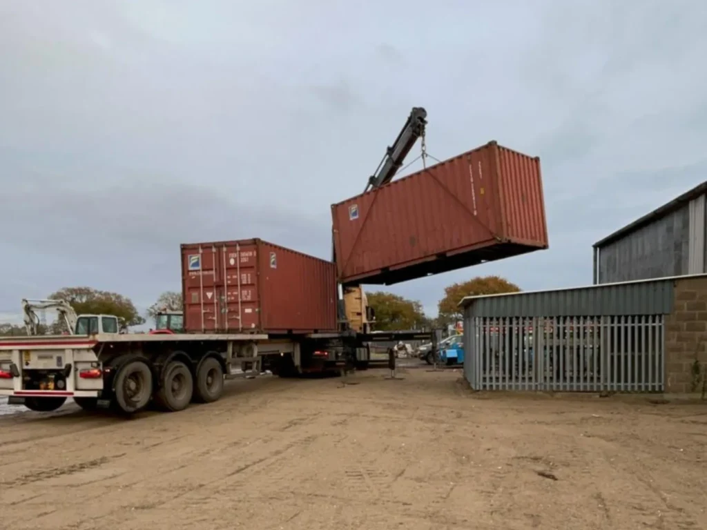 Two 20ft used shipping containers being offloaded by HIAB crane at a farm site