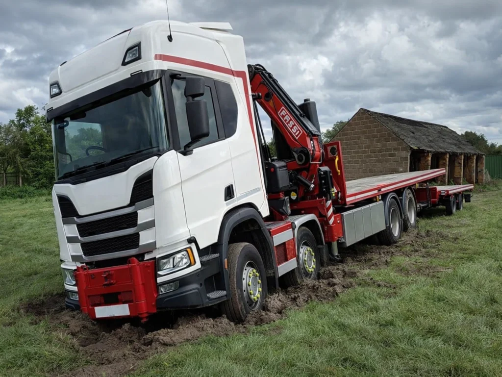 HIAB shipping container lorry sinking into soft grass during UK site delivery, showing why firm ground preparation is essential