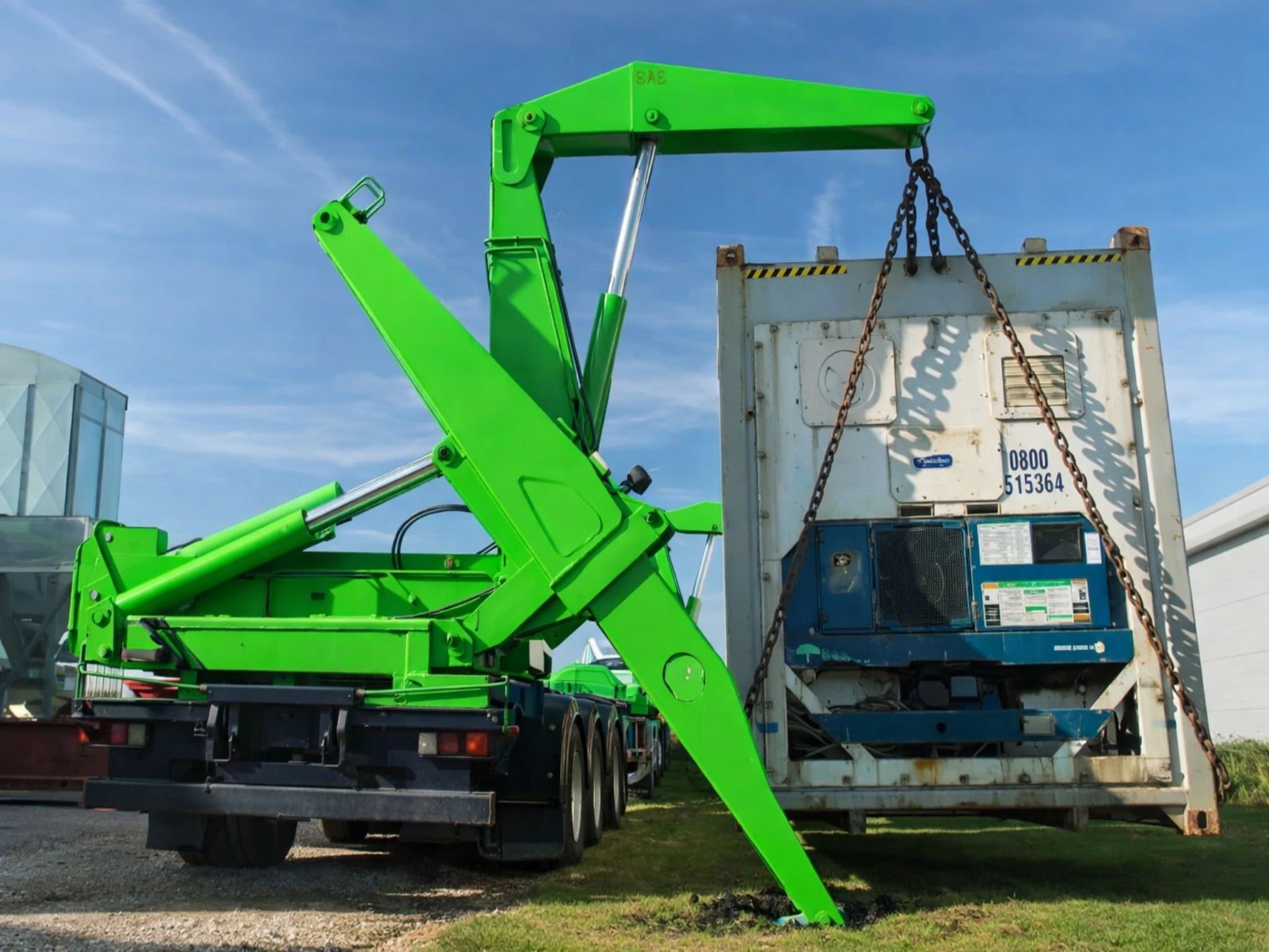 Green sidelifter crane lifting a refrigerated shipping container onto grass, demonstrating HIAB vs sidelifter delivery options in the UK.